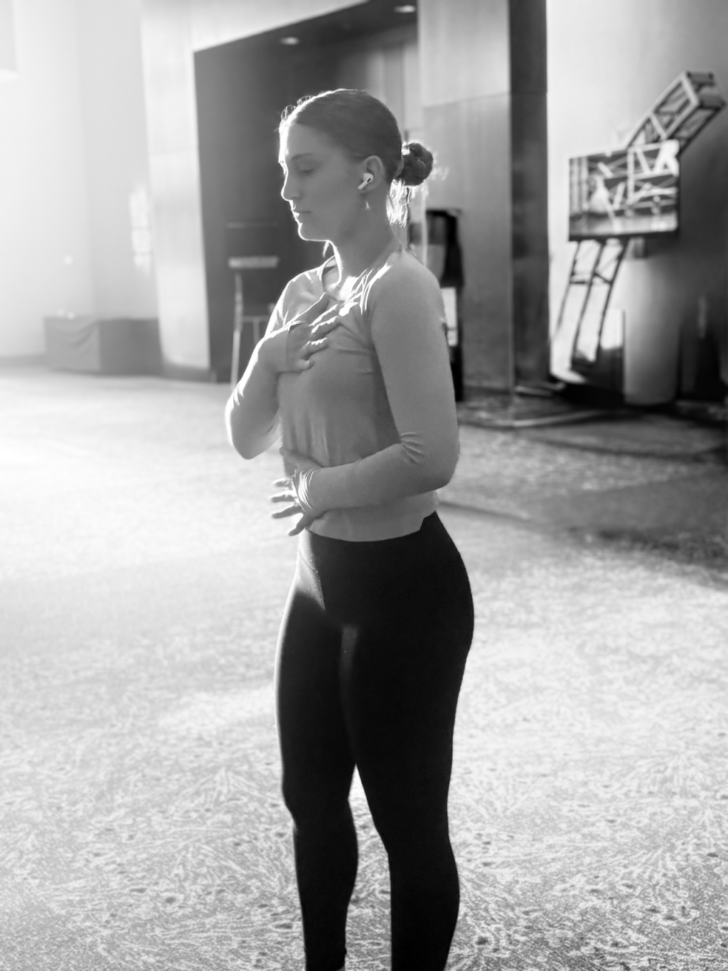 Picture of author's daughter with her earbuds in. Her arms are placed over her heart and stomach and she is taking a deep breath with her eyes closed in preparation to go on stage to perform