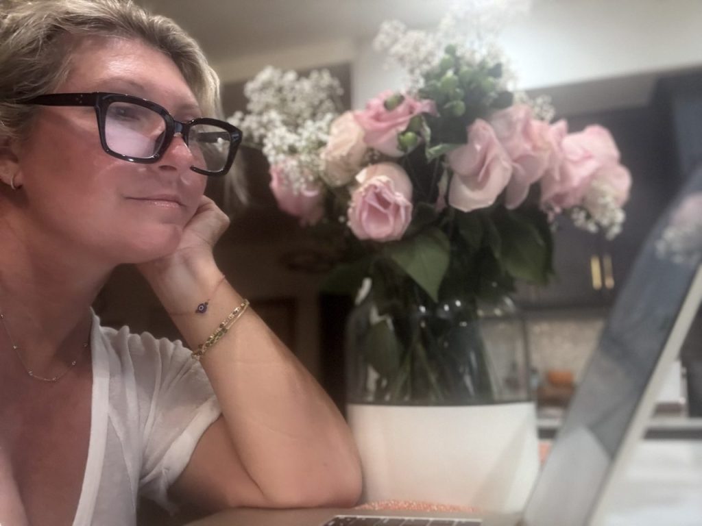 picture of author working on her computer. bouquet of flowers in the background